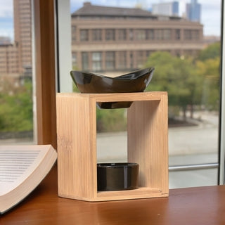 Brûle-parfum Kalos en bambou et céramique noire posé sur un bureau près d'une fenêtre avec vue sur la ville, boutique KAVERN.