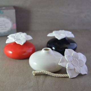 Détail du mécanisme du diffuseur Narcisse : la mèche en coton reliée à la fleur en plâtre, à côté de son vase en céramique blanche.