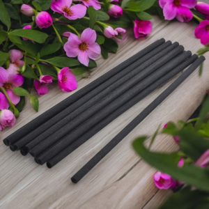 Bouquet de 10 tiges noires en fibre naturelle pour diffuseur de parfum, présentées sur un fond en bois avec des fleurs roses, boutique KAVERN.