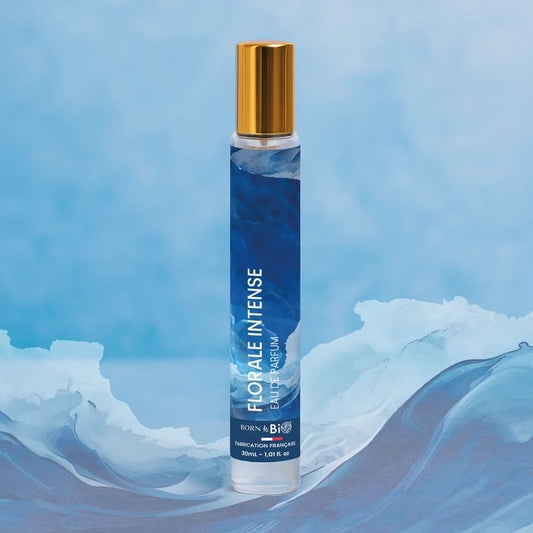 Eau de Parfum Florale Intense Born to Bio au milieu de vagues illustrées. Pyramide olfactive marine : Embruns, Bois Flotté et Bois Ambré.