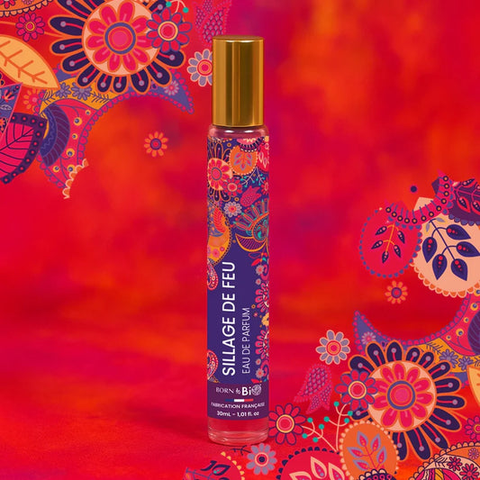 Eau de Parfum Sillage de Feu Born to Bio sur un fond rouge ardent aux motifs floraux. Pyramide olfactive : Jasmin, Bois secs et Poire.