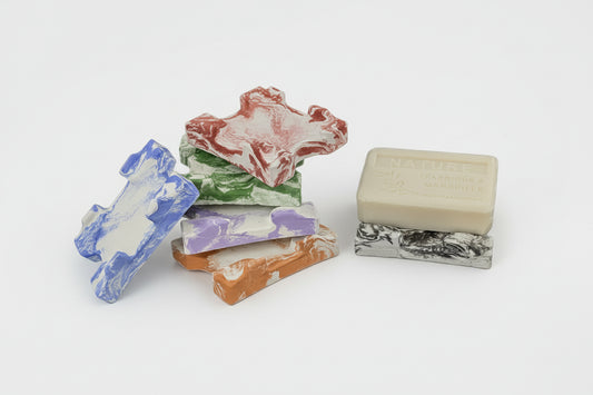 Assortiment de porte-savons artisanaux Mura en ciment marbré de différentes couleurs pour une décoration de salle de bain zéro déchet et élégante.