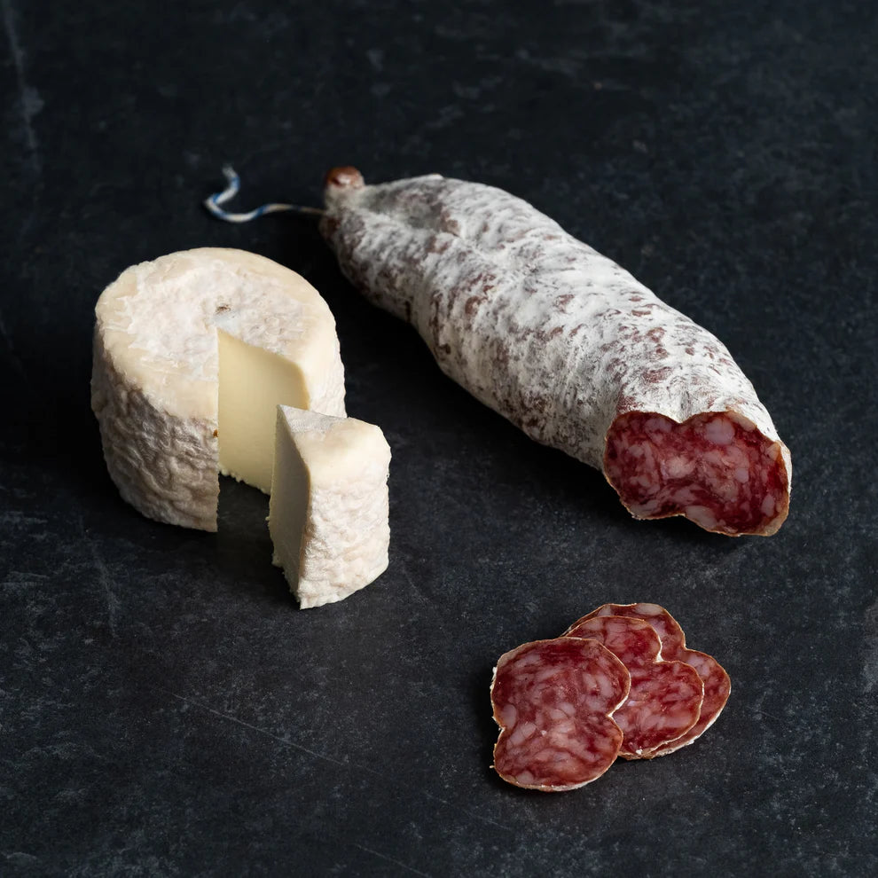 Saucisson sec artisanal pur porc des Cévennes, découpé en tranches fines, présenté à côté d'un délicieux palet de fromage de chèvre.
